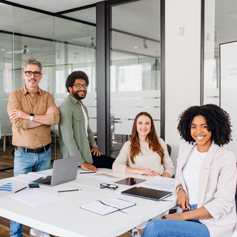 happy coworkers sitting and standing around table in office